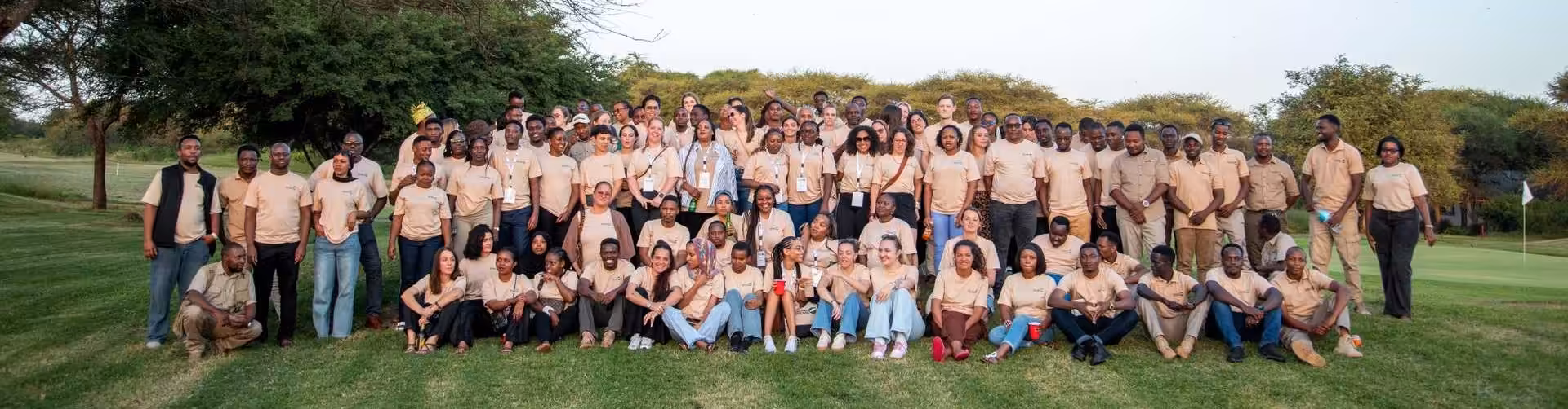 The entire Your Tanzania Trip team gathered outdoors for a group photo, standing and sitting together on a green lawn surrounded by nature.
